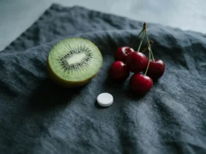 Doorgesneden kiwi en tarte kersen naast een wit magnesiumtablet op donker linnen, rustgevende flatlay.